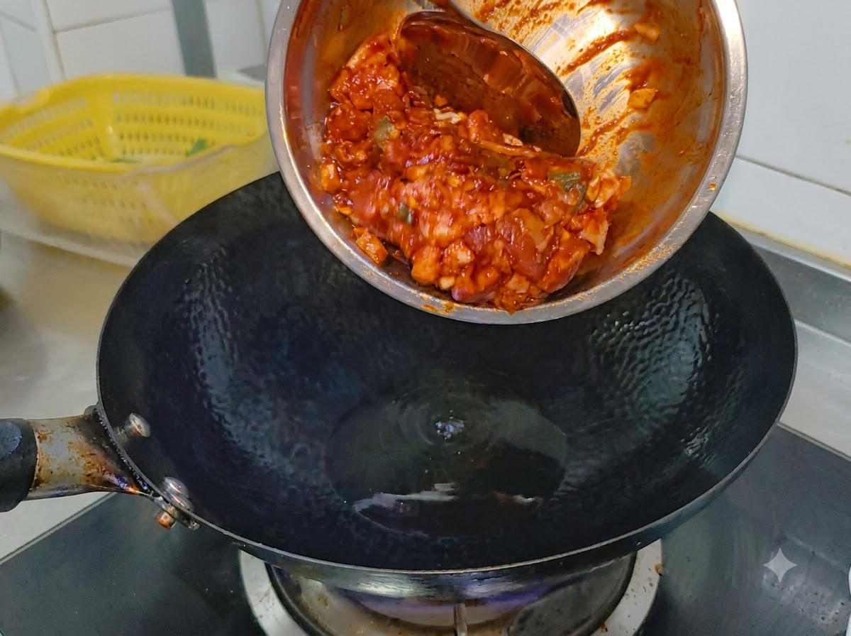 Poitrine de porc pimentée et marinée glissant dun bol en métal vers un wok noir très chaud contenant de lhuile de cuisson.