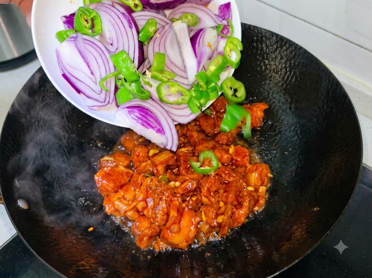 Tranches doignon violet et de piments verts versées depuis une assiette blanche dans un wok où cuit la poitrine de porc.
