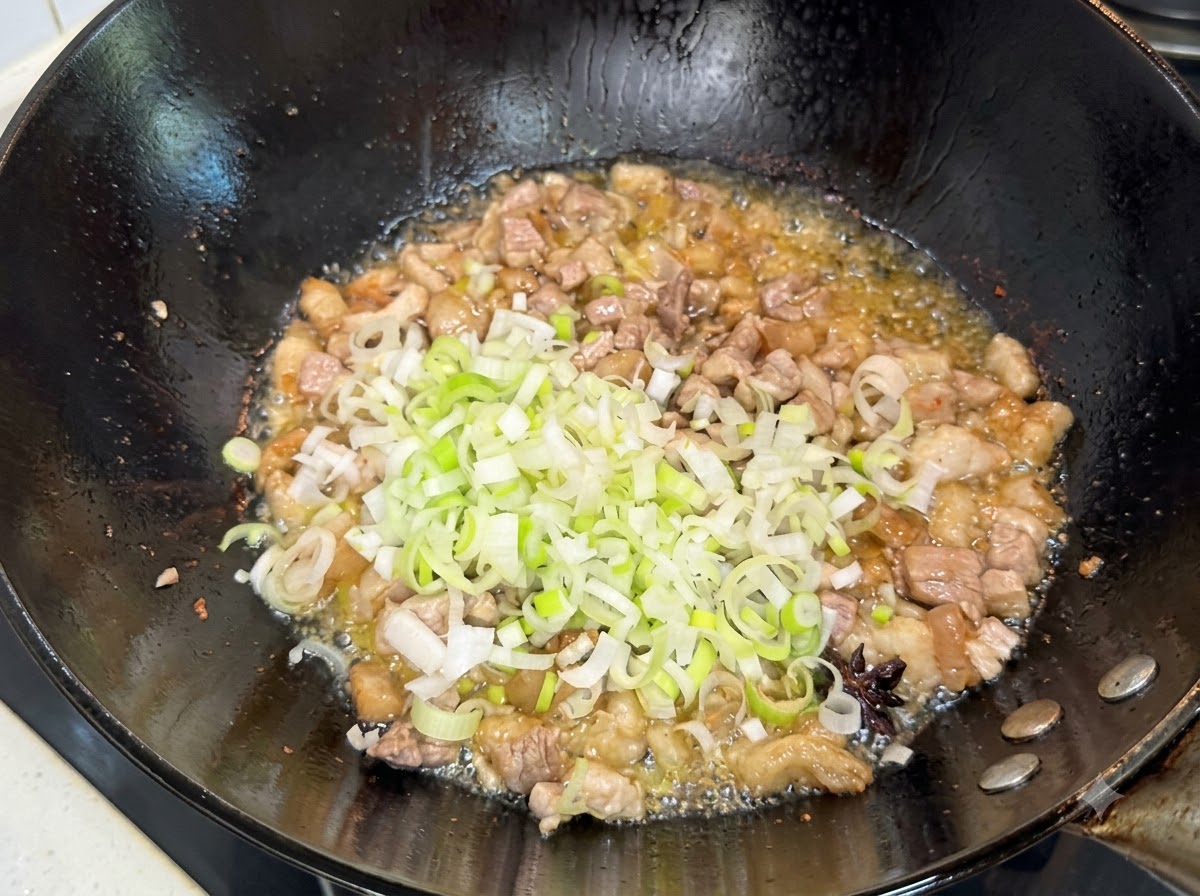 Oignons nouveaux verts hachés incorporés au mélange de porc doré dans le wok.