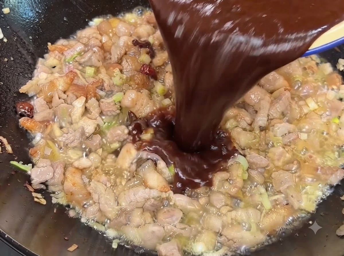 Mélange de sauce à base de pâte de soja foncée et de haricots doux versé dans le wok sur le porc cuit.