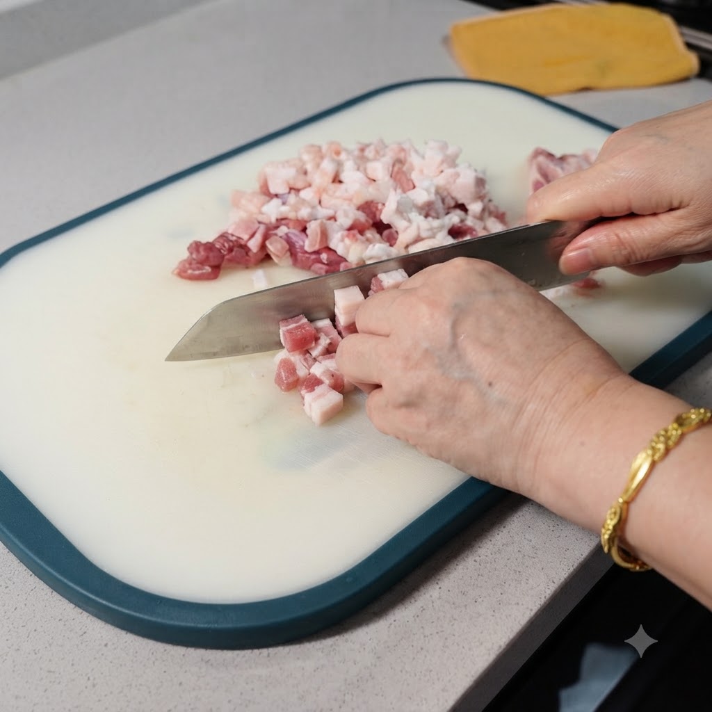 Un gros plan de poitrine de porc crue en cours de découpe en petits cubes avec un couteau sur une planche à découper blanche.