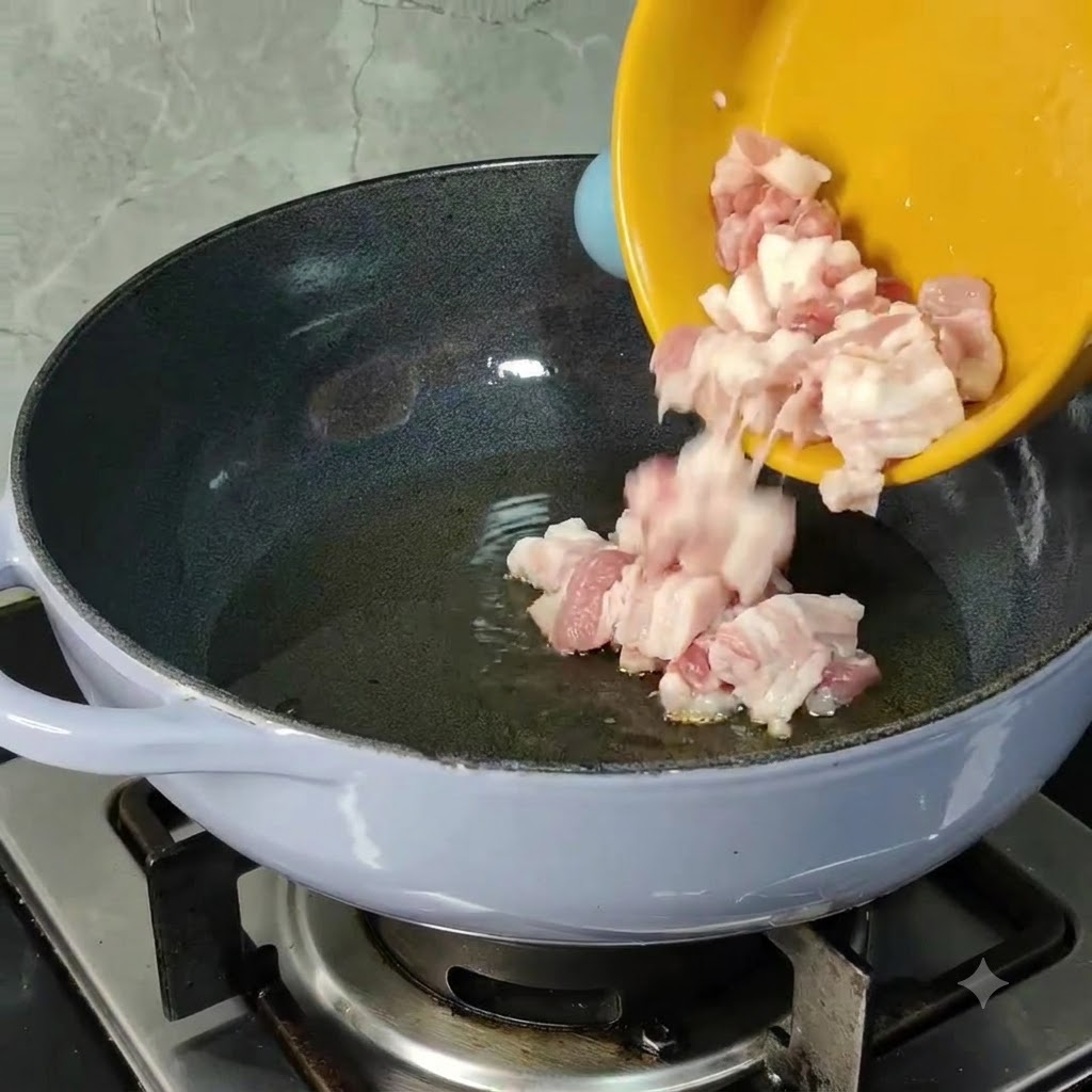 Des morceaux de poitrine de porc crue glissant dun bol jaune vers une poêle chauffée contenant de lhuile de cuisson.