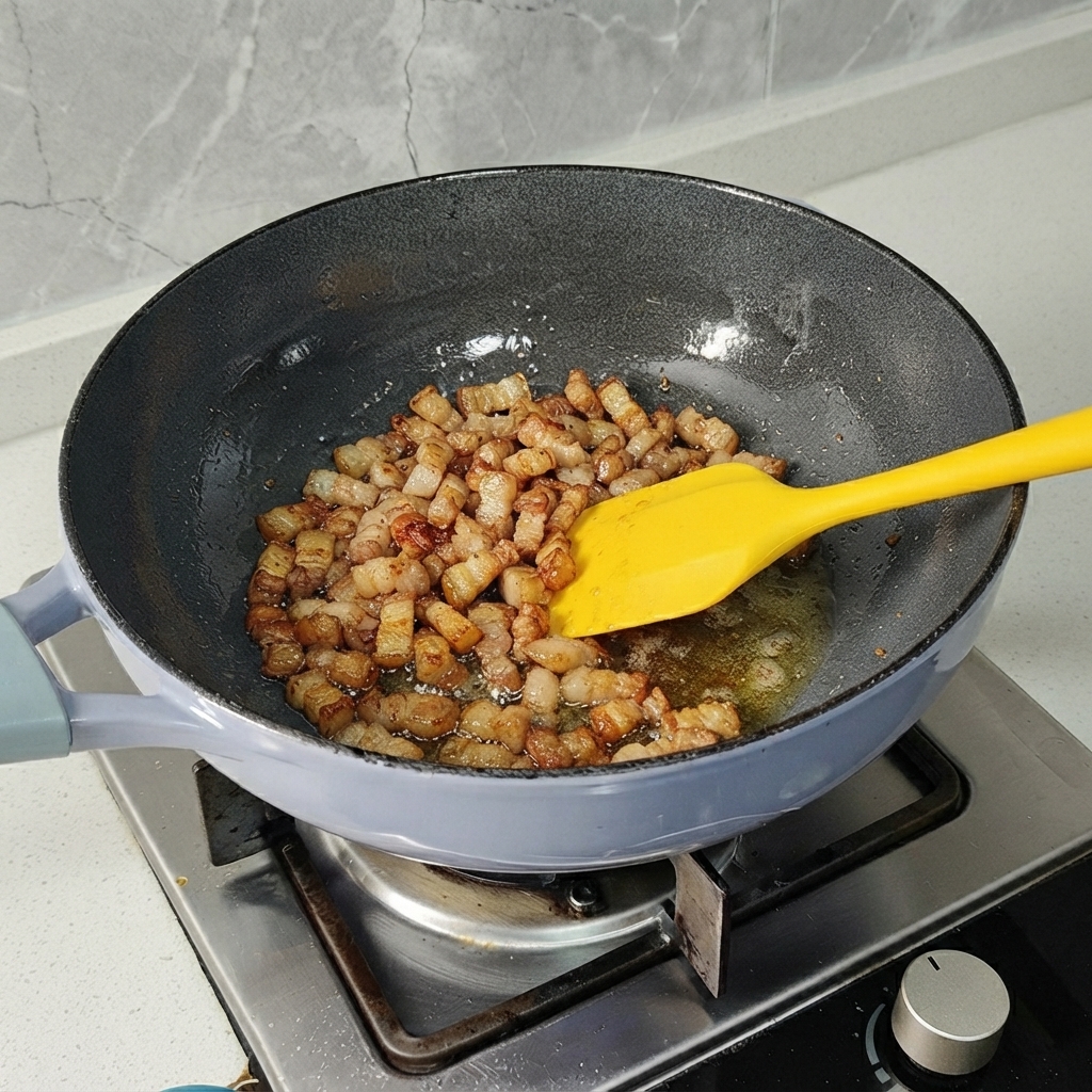 Des morceaux de poitrine de porc sautés dans une poêle avec une spatule jaune jusquà ce quils soient légèrement dorés.