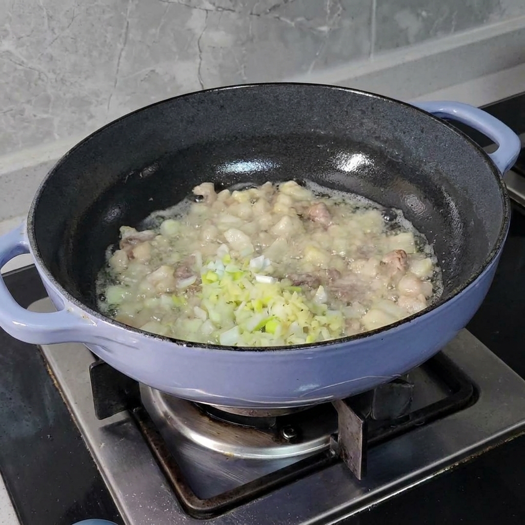 De la ciboulette, du gingembre et de lail finement hachés ajoutés aux morceaux de porc grésillants dans une poêle sombre.