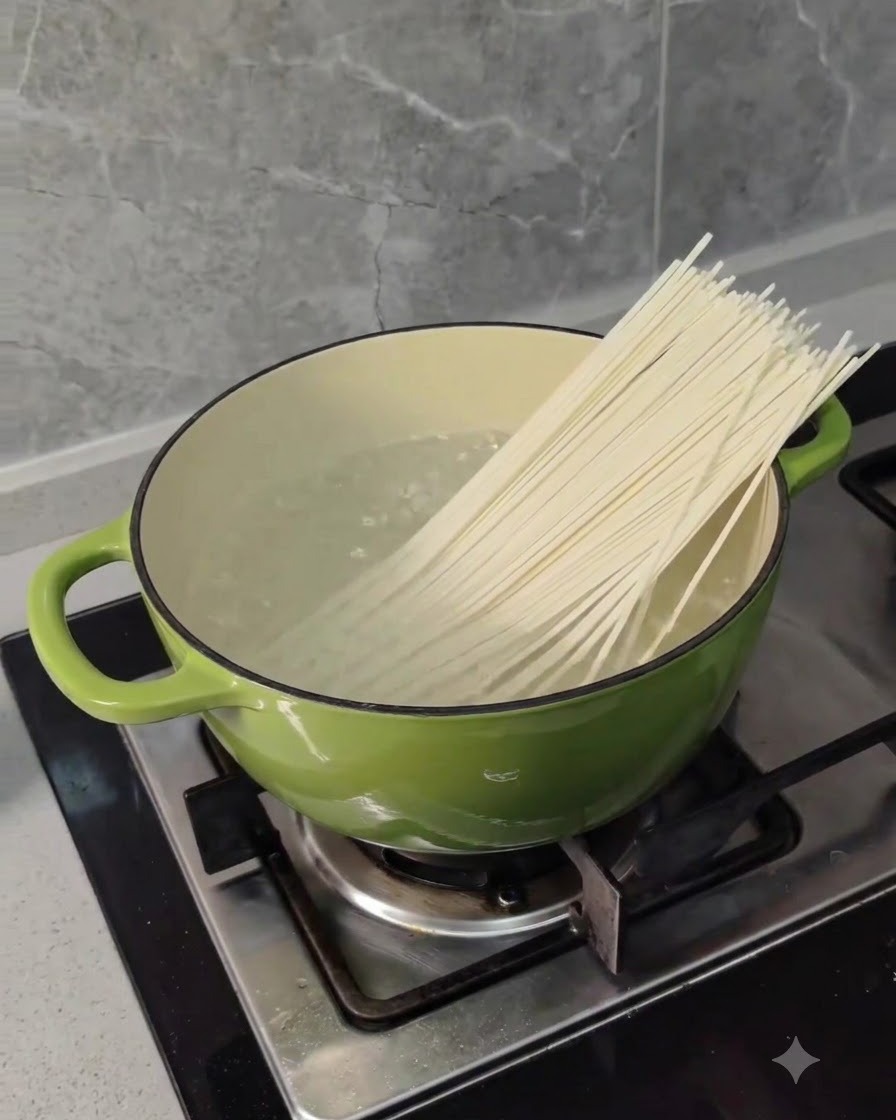 De longues nouilles de blé sèches plongées dans une casserole verte deau bouillante sur une cuisinière.