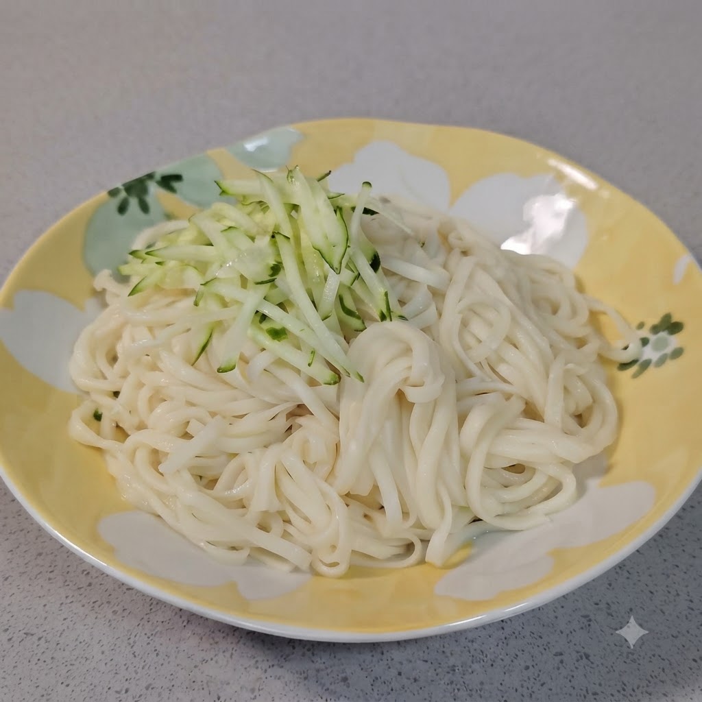 Un petit dôme de concombre vert frais râpé disposé sur des nouilles blanches bouillies dans une assiette décorative.