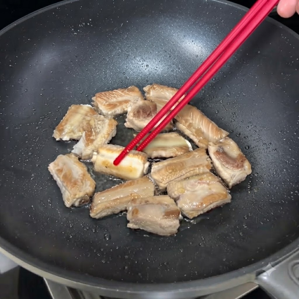 Travers de porc grésillant dans une poêle, retournés avec des baguettes pour dorer uniformément.