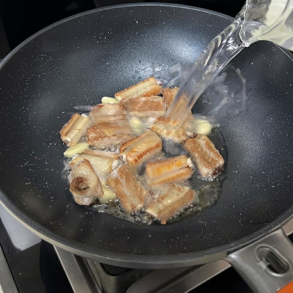Eau versée depuis un bol dans la poêle crépitante contenant les travers et lail.