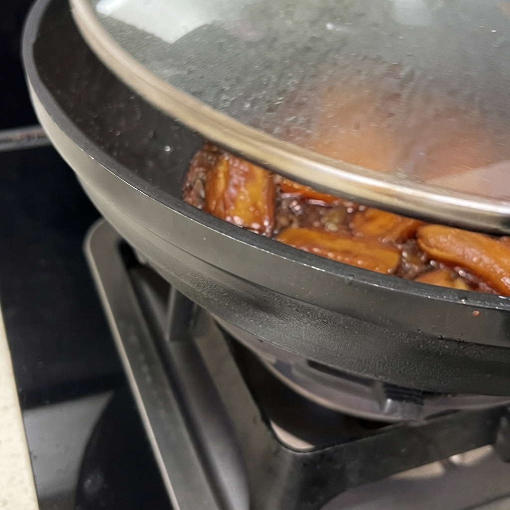 Gros plan dun wok au couvercle partiellement soulevé, montrant les travers de porc dans une sauce brune réduite et brillante.