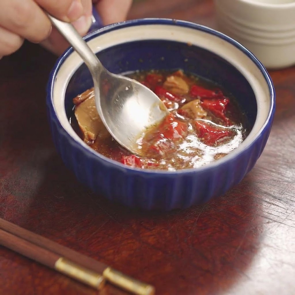 Une cuillère écrasant et mélangeant du tofu rouge fermenté et des assaisonnements à lintérieur dun petit bol en céramique bleue.