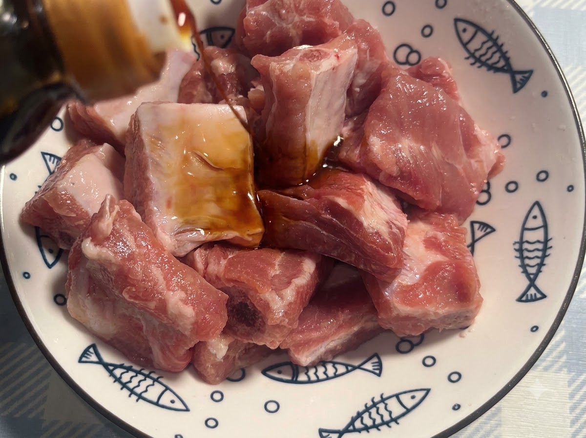 Travers de porc dans un bol blanc à motifs assaisonnés avec de la sauce soja noire.
