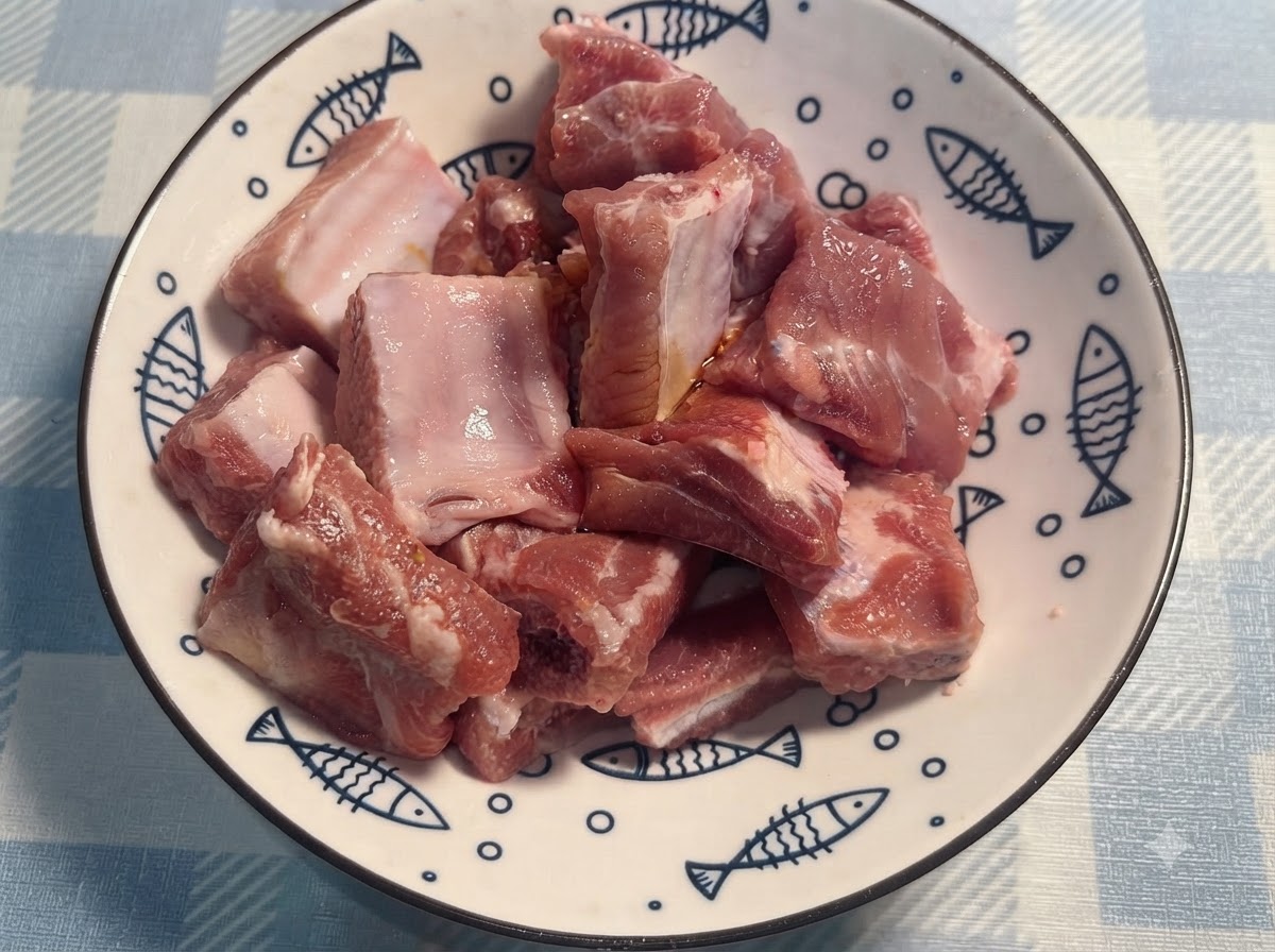 Des mains gantées mélangeant les travers de porc assaisonnés dans une assiette blanche.