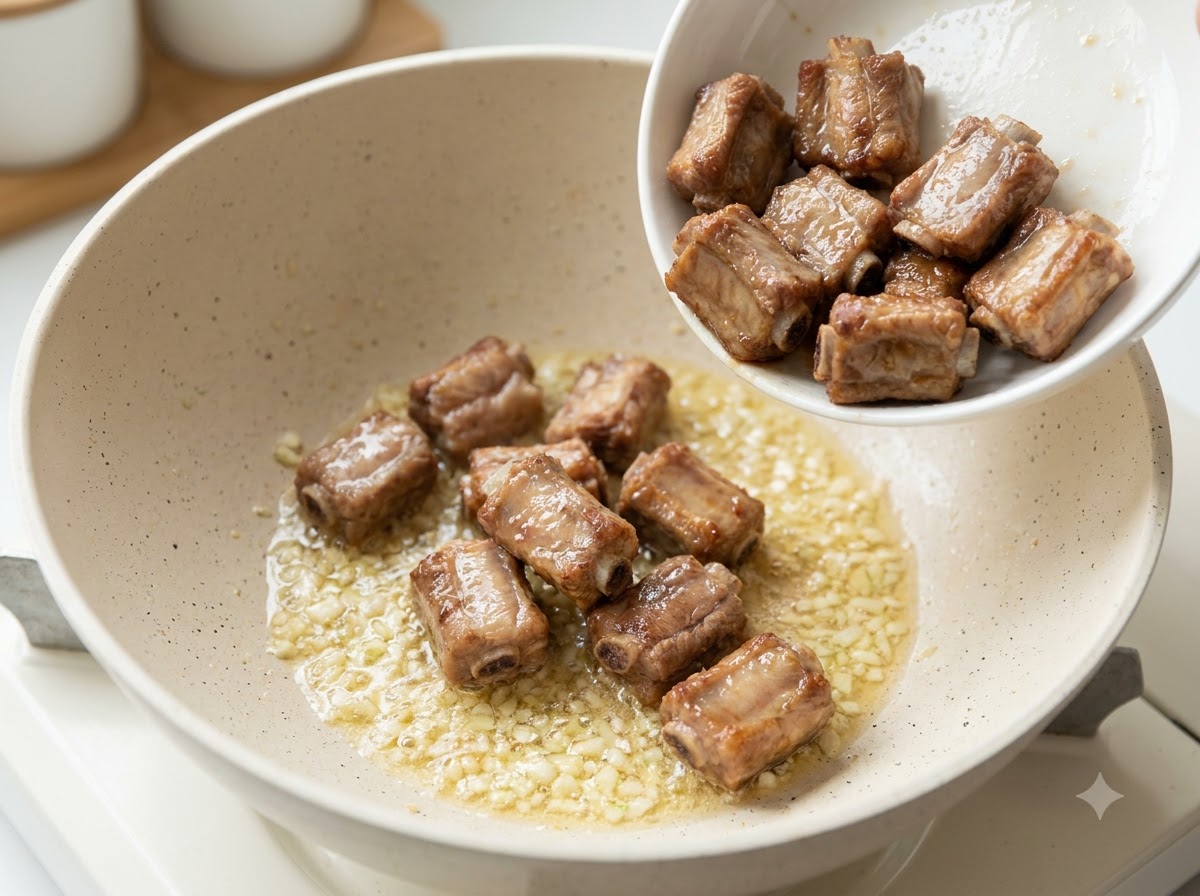 Travers de porc poêlés versés dans une poêle contenant de lail haché sauté et du beurre.