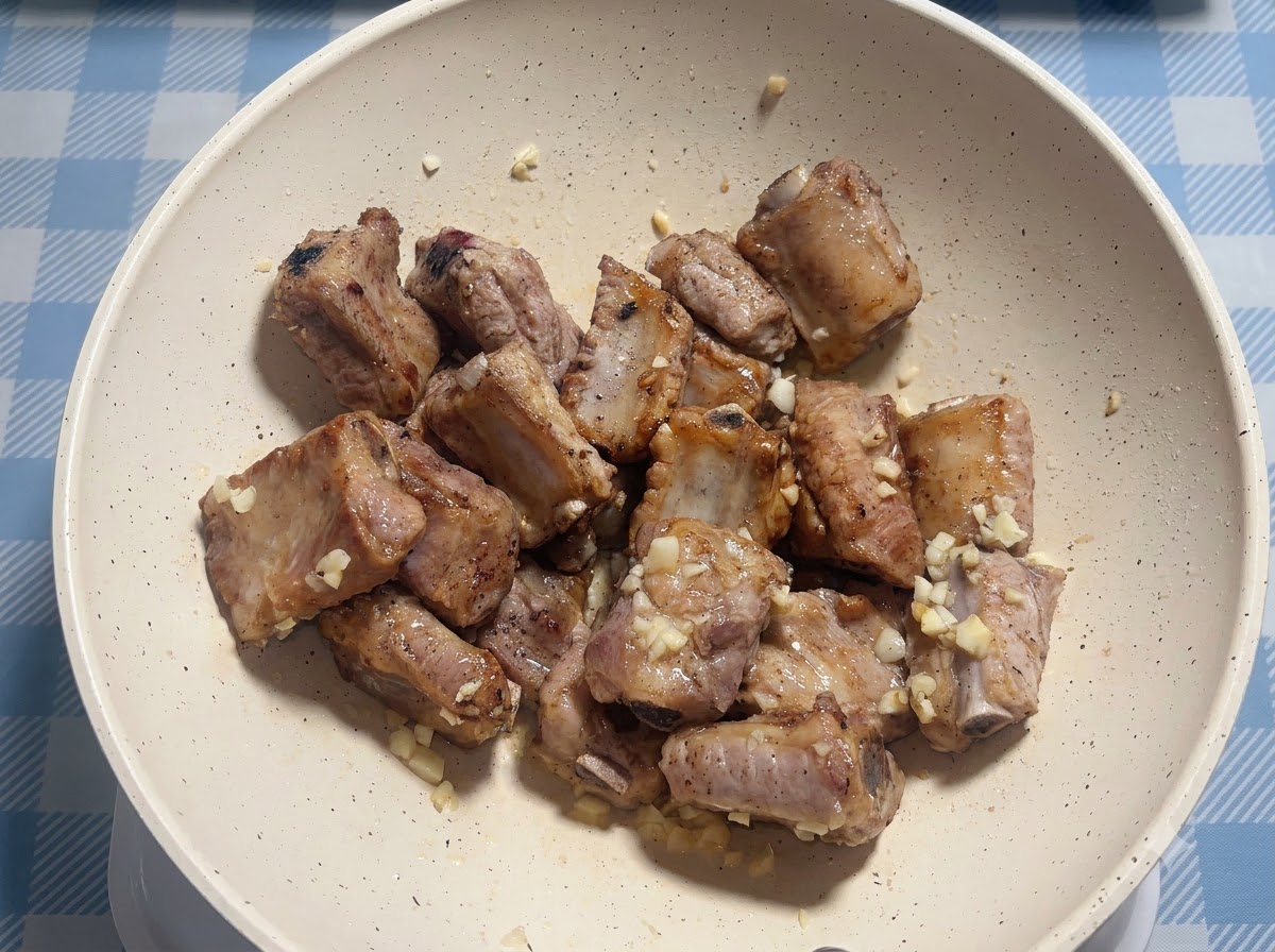 Travers de porc assaisonnés de sauce dans une poêle blanche.