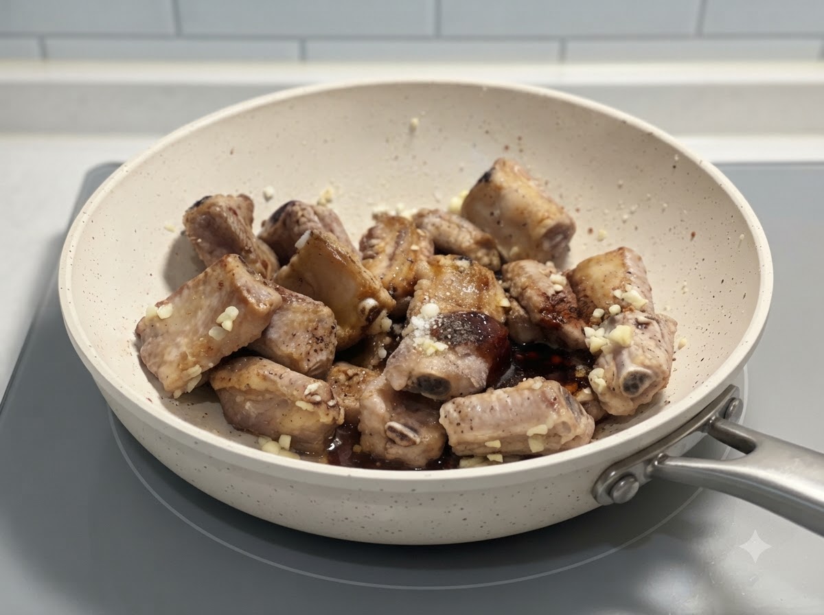Travers de porc mélangés avec des assaisonnements et de lail haché dans une poêle blanche sur une cuisinière.
