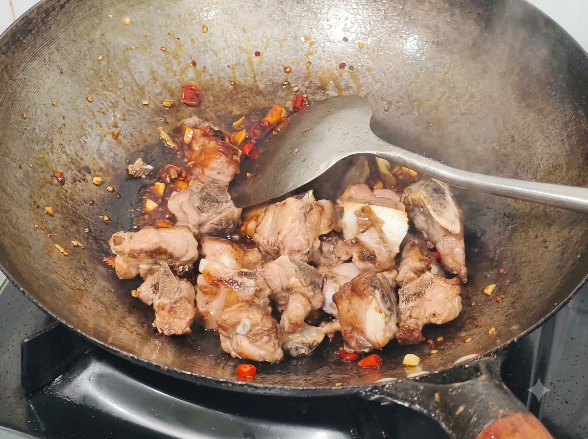 Travers de porc frits enrobés de sauce, de piments hachés et dail dans le wok à laide dune spatule en métal.