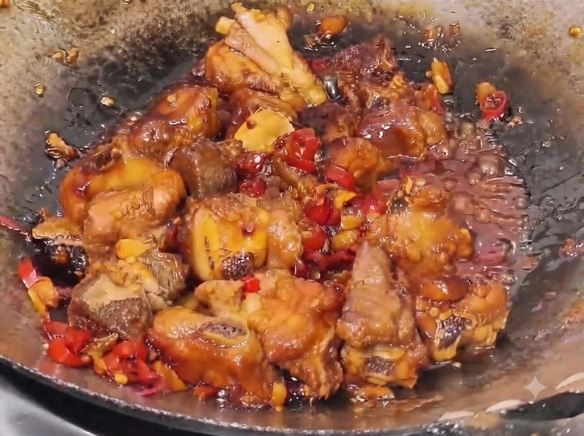 Travers de porc mijotant dans une sauce épaisse et sombre avec des morceaux de piment rouge et dail visibles dans un wok.