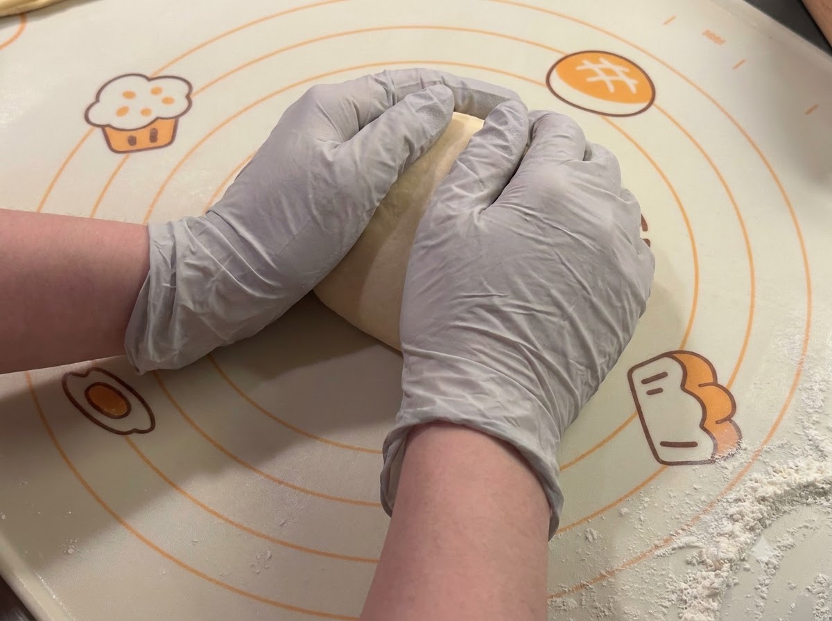 Mains gantées façonnant et arrondissant des portions de pâte sur un tapis de cuisson.