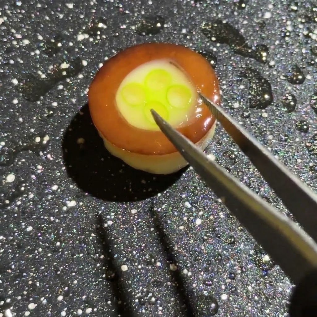 Une paire de pinces ajoutant du jambon, des oignons et des champignons colorés coupés en dés sur la base dœuf et de ciboulette à lintérieur de lanneau de champignon.