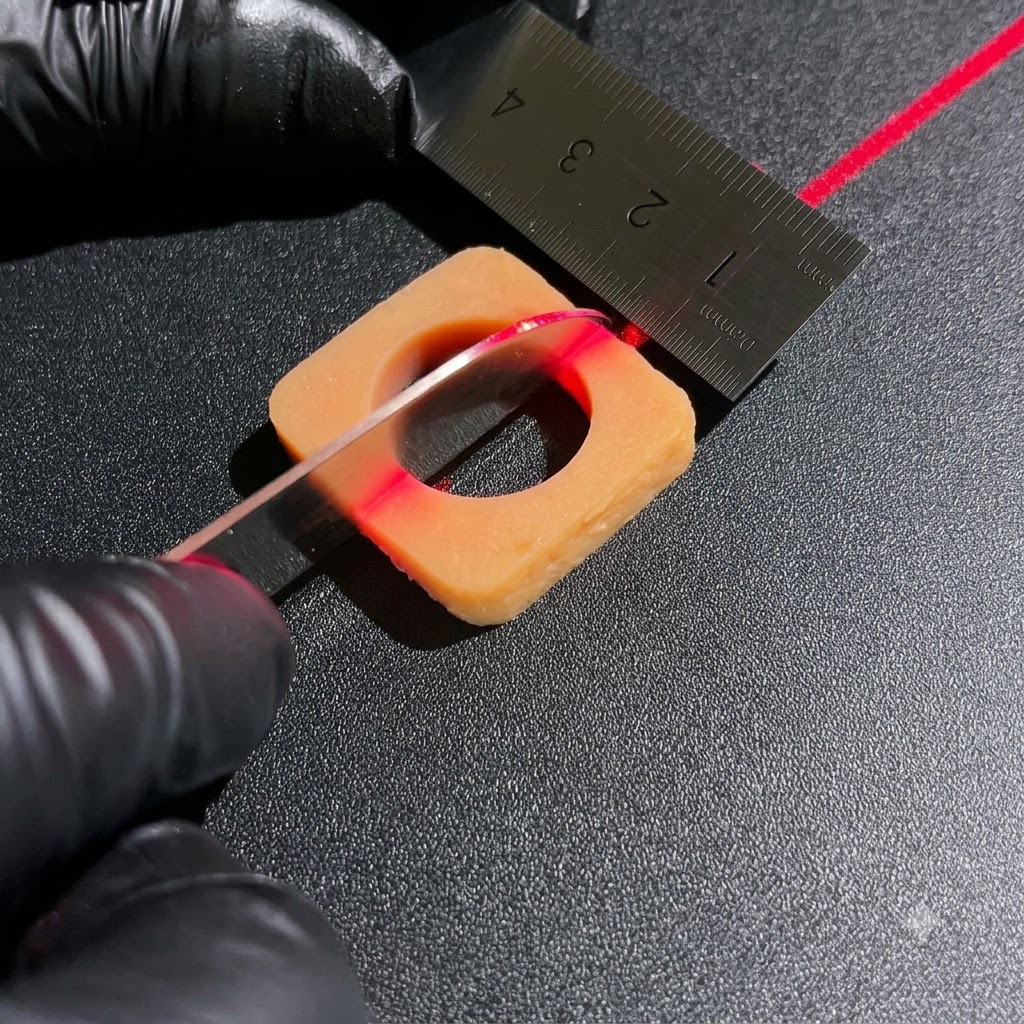 Des mains gantées utilisant un couteau bien aiguisé et une règle en métal pour couper des blocs dingrédients carrés sous une ligne dalignement laser rouge.