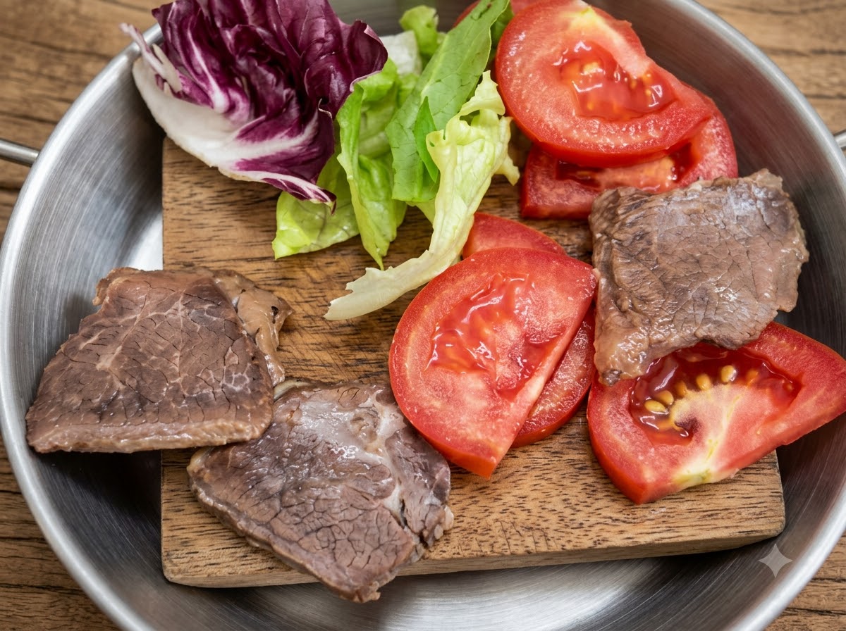 Laitue fraîche, tomates tranchées et morceaux de viande cuits disposés sur une petite planche en bois.
