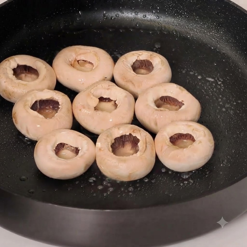 Chapeaux de champignons de Paris entiers en train de frire dans une poêle huilée avec de lassaisonnement au poivre.