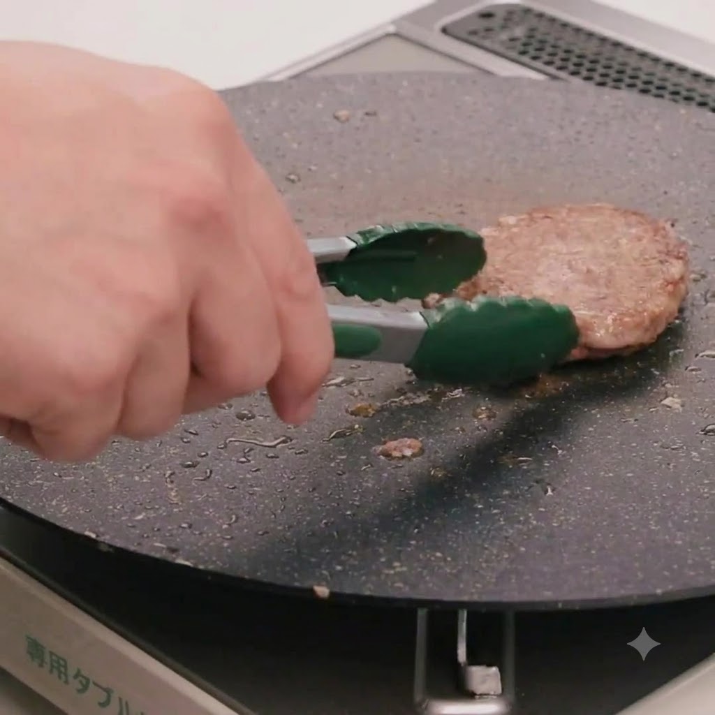 Une main utilisant des pinces de cuisine vertes pour retourner un steak de bœuf cuisant dans une poêle plate.