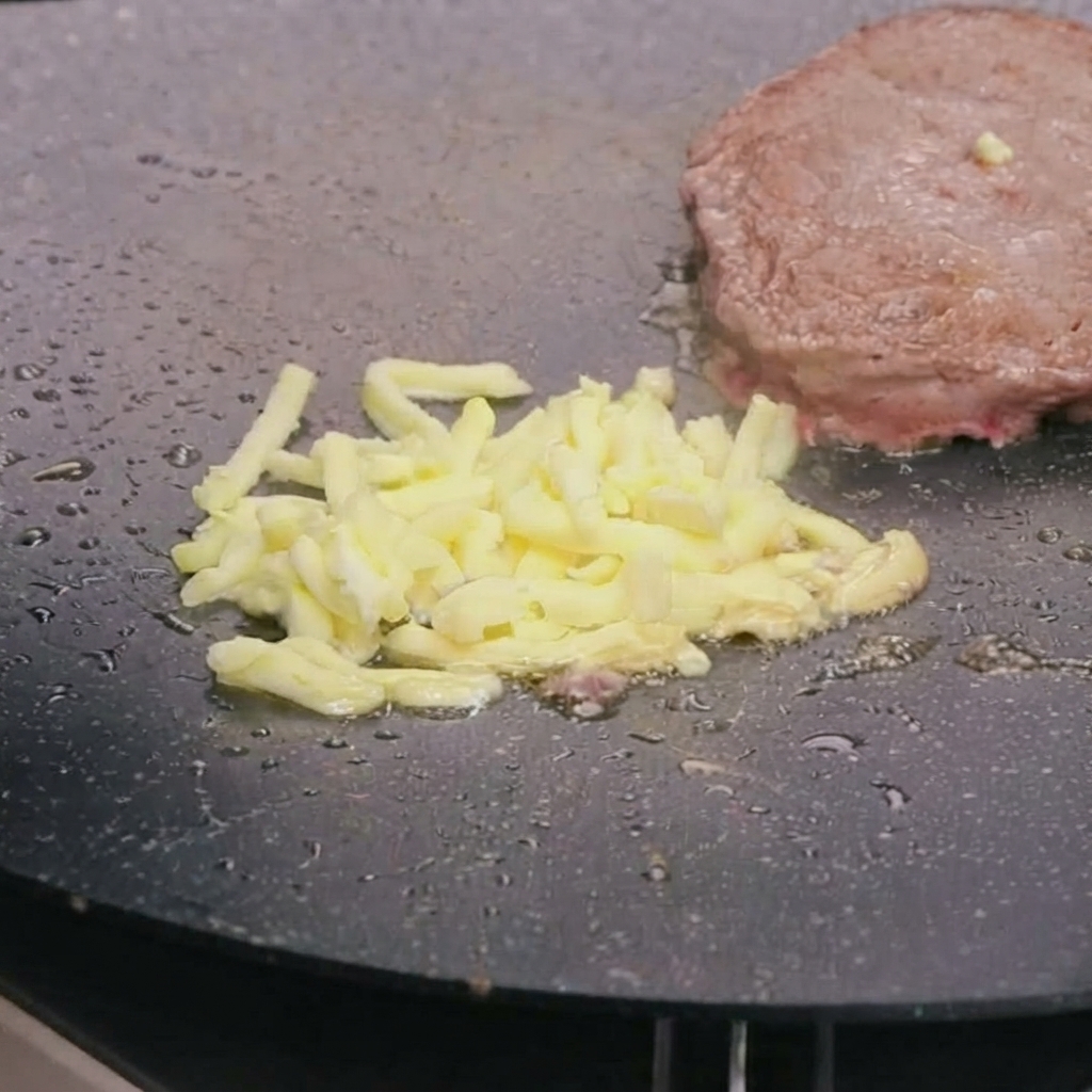Du fromage mozzarella râpé fondant sur le dessus dun steak de bœuf poêlé dans une poêle chaude.