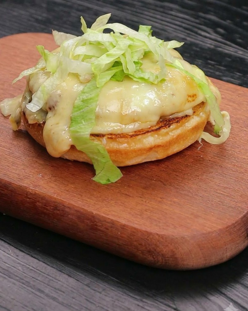 De la laitue fraîche émincée disposée proprement sur un steak de bœuf au fromage fondu reposant sur une base de pain toasté.