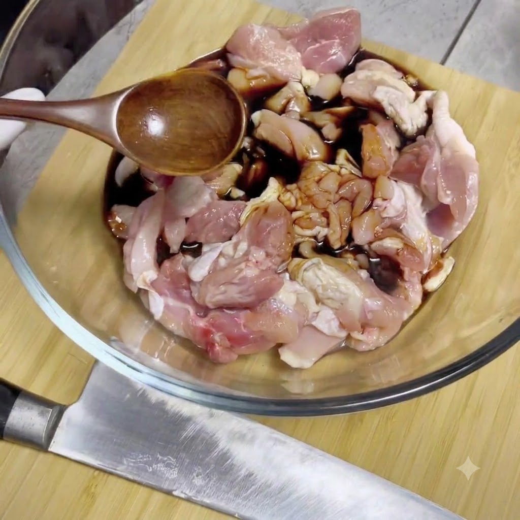 De la sauce soja versée à partir dune cuillère en bois sur des morceaux de poulet crus à lintérieur dun bol mélangeur en verre.