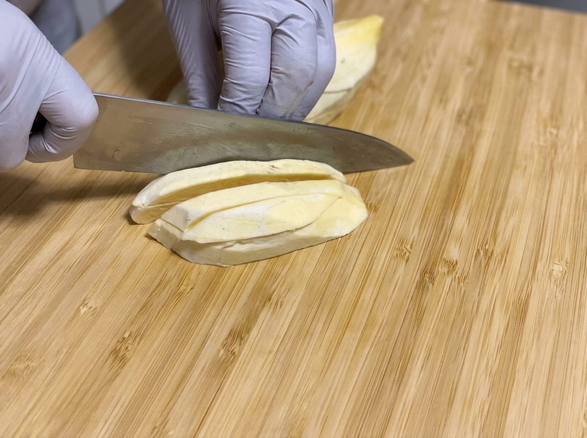 Des patates douces crues pelées coupées en longs bâtonnets avec un couteau sur une planchette à découper en bois.