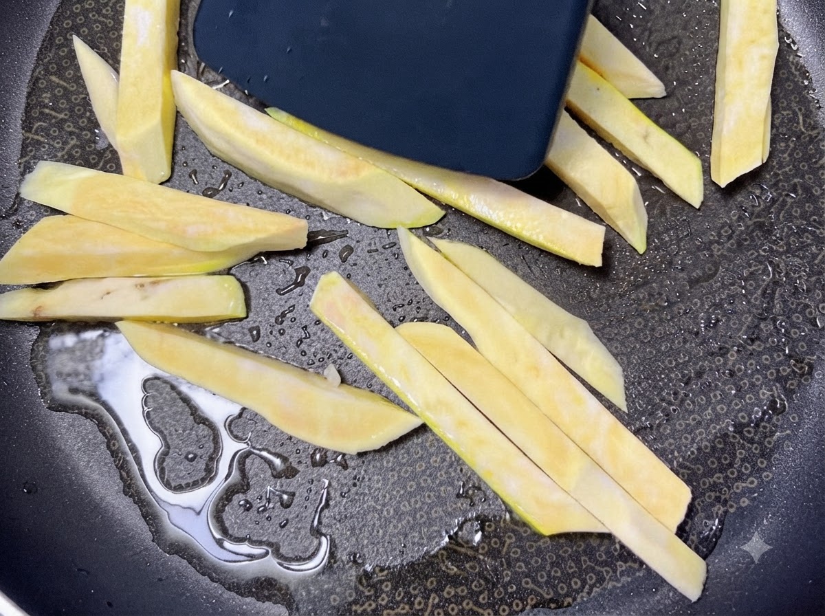 Des bâtonnets de patate douce crus grésillant dans une poêle noire chauffée avec de lhuile tout en étant déplacés avec une spatule.