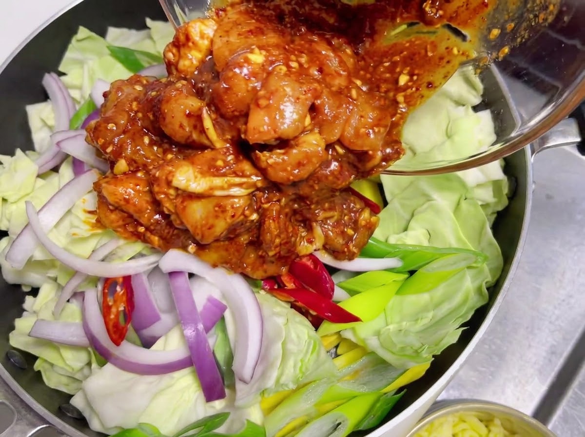 Du poulet cru mariné enrobé de sauce rouge piquante versé dun bol en verre sur un lit de chou cru et doignons.