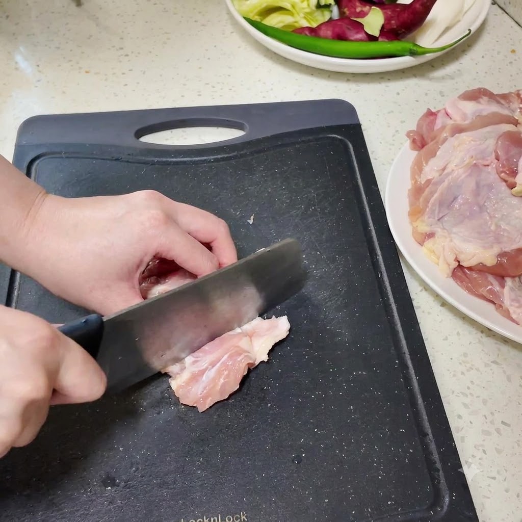 Des pilons de poulet désossés en cours de découpe en petits morceaux sur une planche à découper noire.