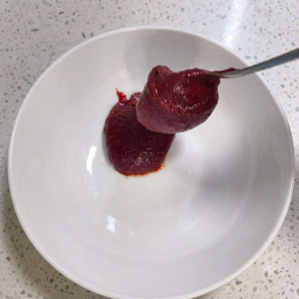 De la pâte de piment coréenne et dautres assaisonnements en cours de mélange à lintérieur dun bol blanc.