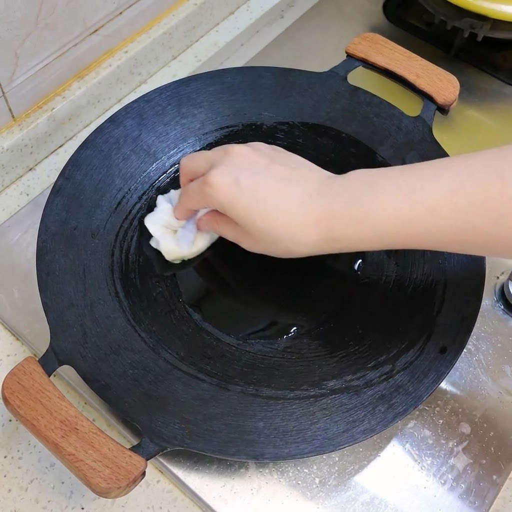 Un wok foncé en cours de huilage ou dessuyage avec un chiffon blanc sur une table de cuisson.