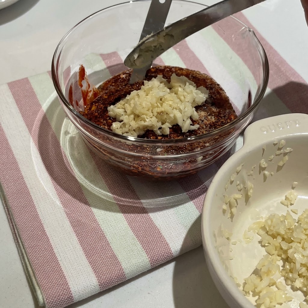 De la pâte de piment coréenne et divers condiments mélangés dans un bol en verre pour former une sauce rouge épaisse.