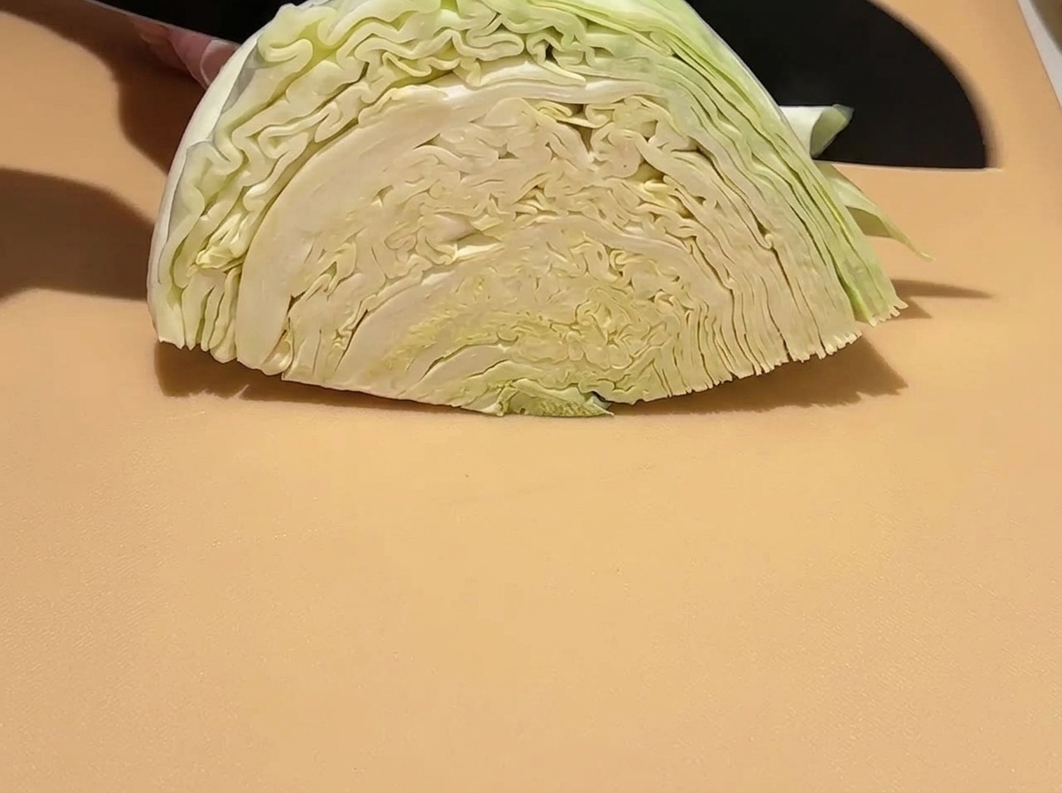 Un quartier de chou vert cru en train dêtre découpé en morceaux plus petits sur une planche à découper avec un couteau.