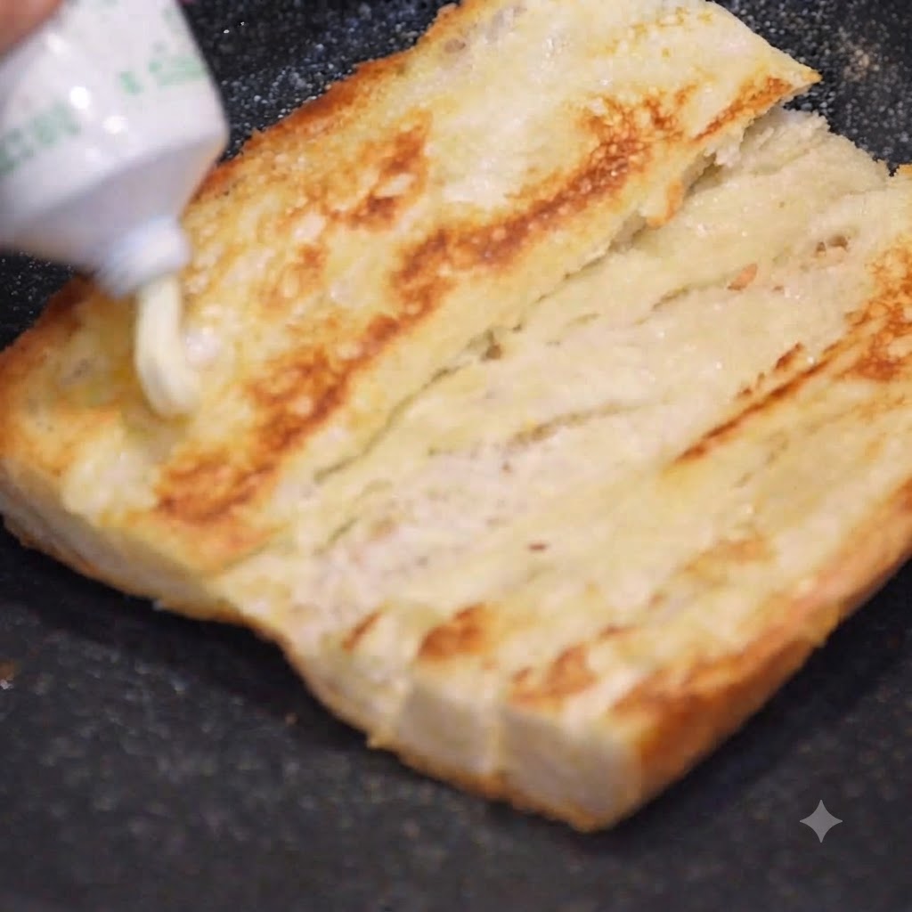 De la mayonnaise pressée dun tube sur une moitié de baguette dorée et toastée.
