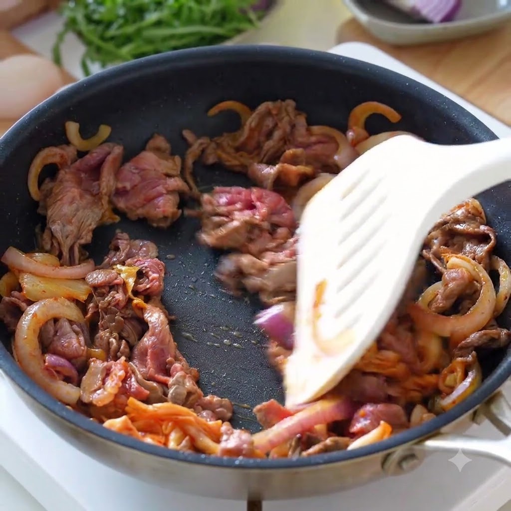 Bœuf émincé, oignons et kimchi mélangés dans une poêle avec une spatule.