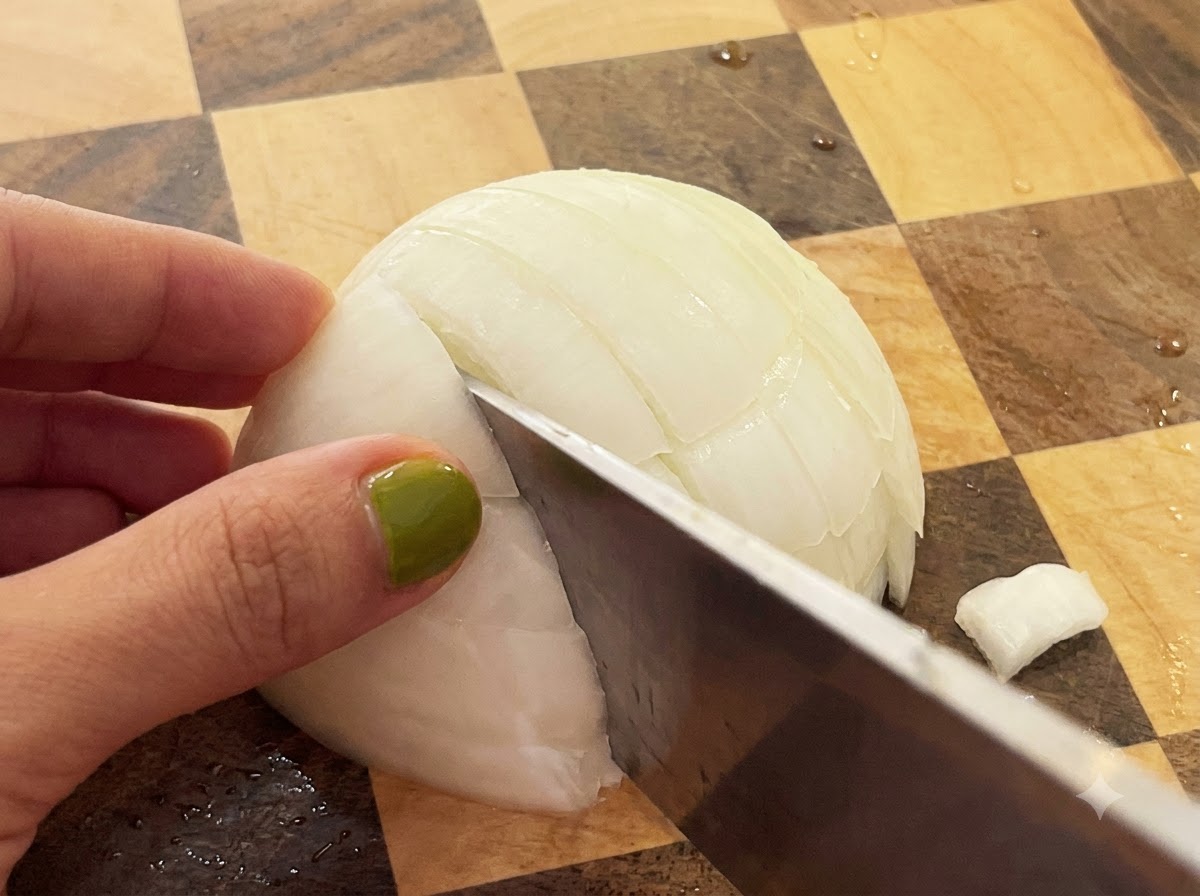 Un couteau coupant à travers un oignon blanc coupé en deux sur une planche à découper en bois à damier.