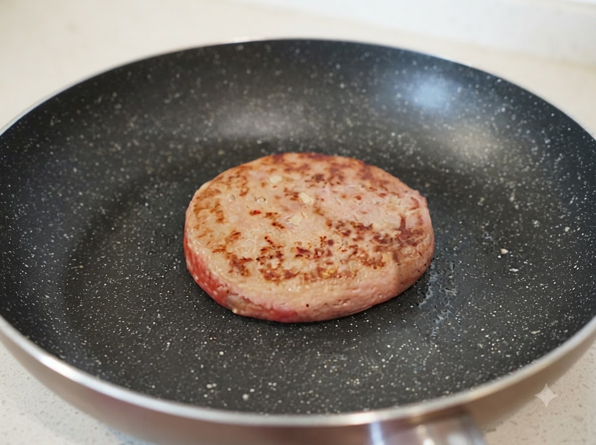 Un petit filet deau versé dans une poêle à côté dun steak haché partiellement dorées.