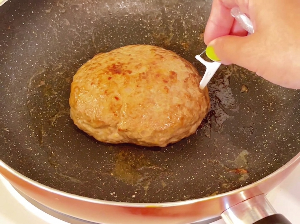 Un cure-dent inséré dans la surface supérieure dun steak haché épais et cuit dans une poêle.