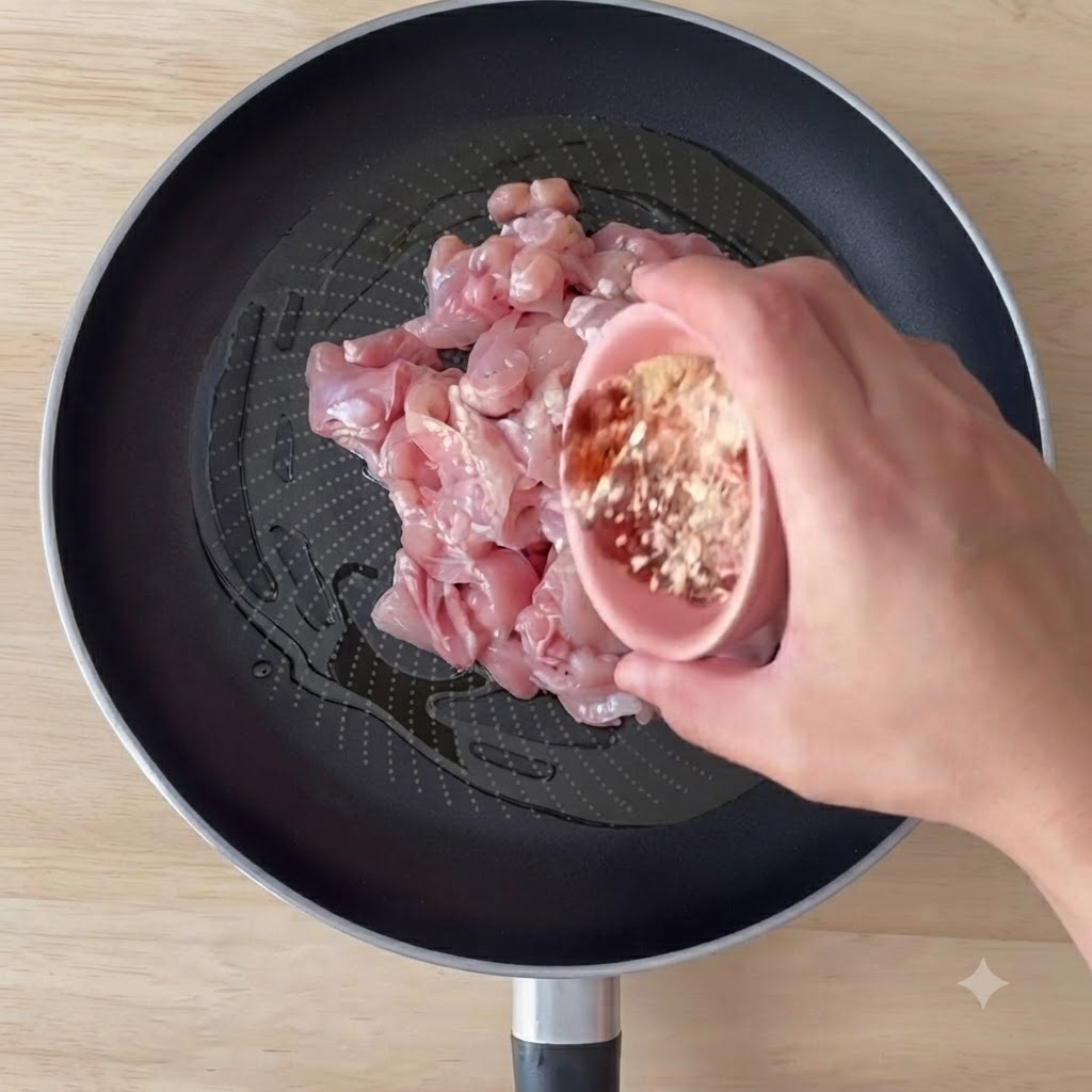 Morceaux de poulet désossés en train de cuire dans une poêle avec de lhuile dolive et des épices en cours de mélange.