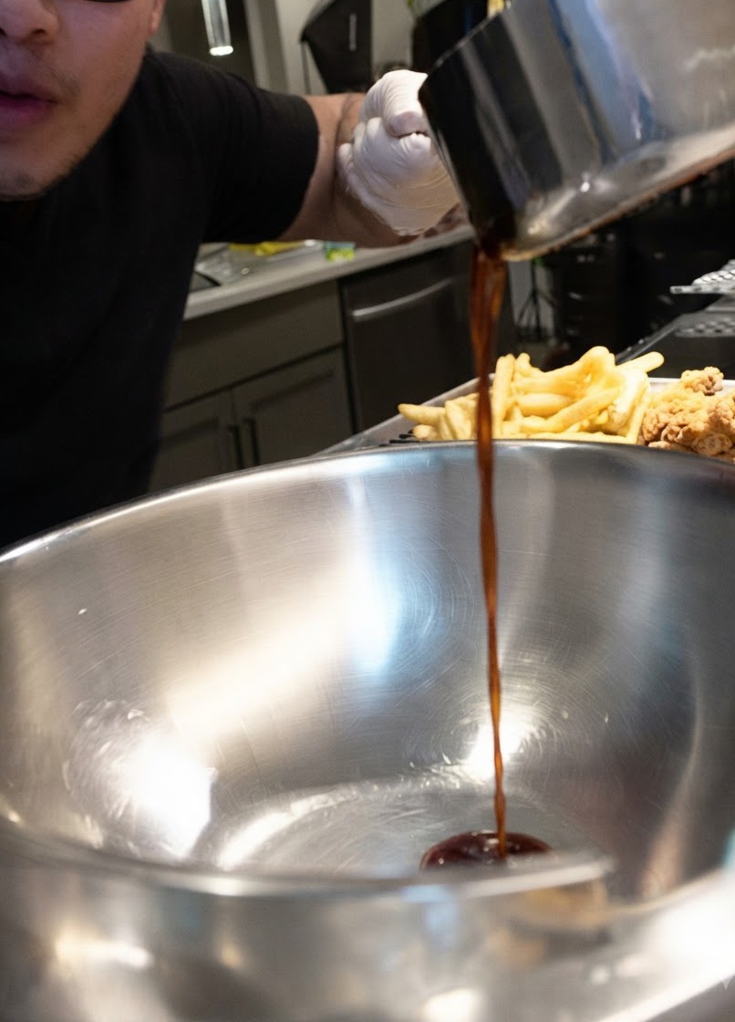 De la sauce foncée versée en un flux régulier dune casserole dans un grand bol en acier inoxydable à côté de morceaux de poulet frit.