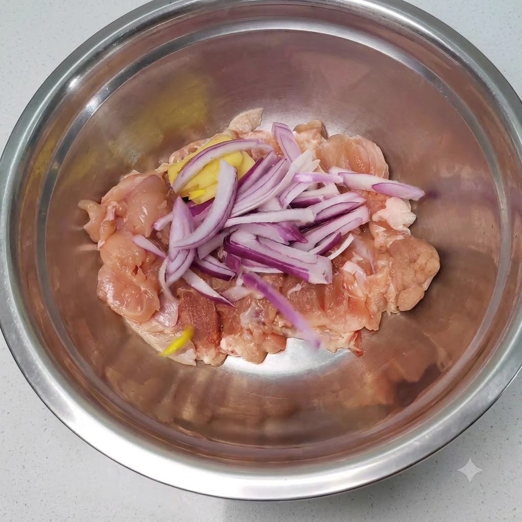 Morceaux de poulet crus mélangés à des tranches doignons rouges et de gingembre dans un bol mélangeur en acier inoxydable.