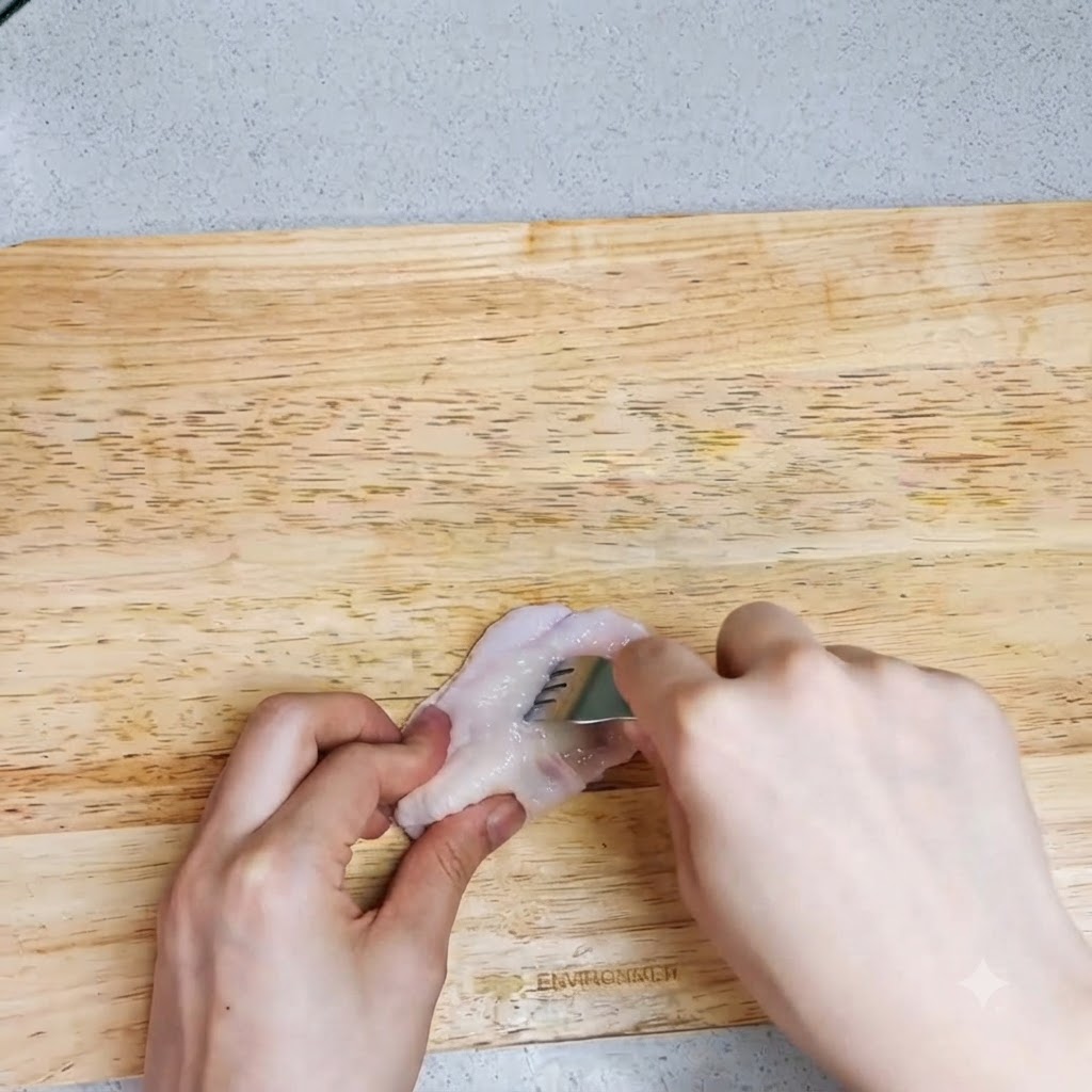 Une paire de mains utilisant une fourchette pour percer des trous dans une aile de poulet crue sur une planche à découper.