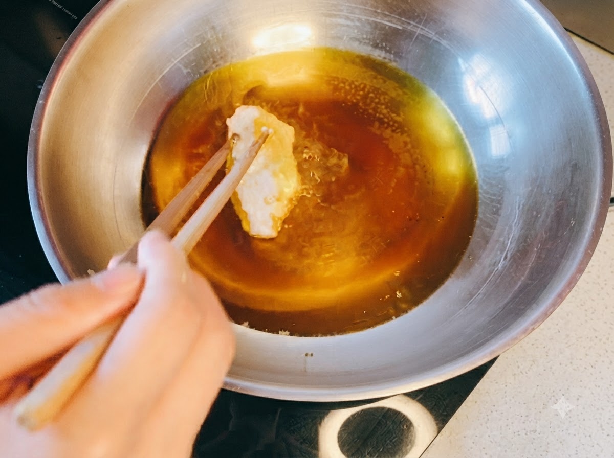 Des baguettes plaçant un morceau de poulet pané dans une poêle en métal remplie dhuile chaude.