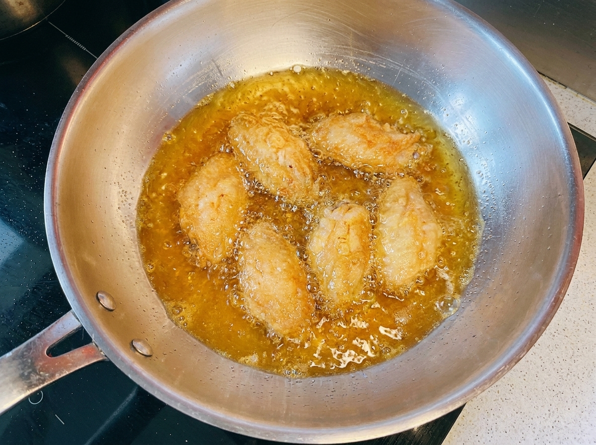 Ailes de poulet dorées en train de frire dans lhuile chaude à lintérieur dune poêle en métal.
