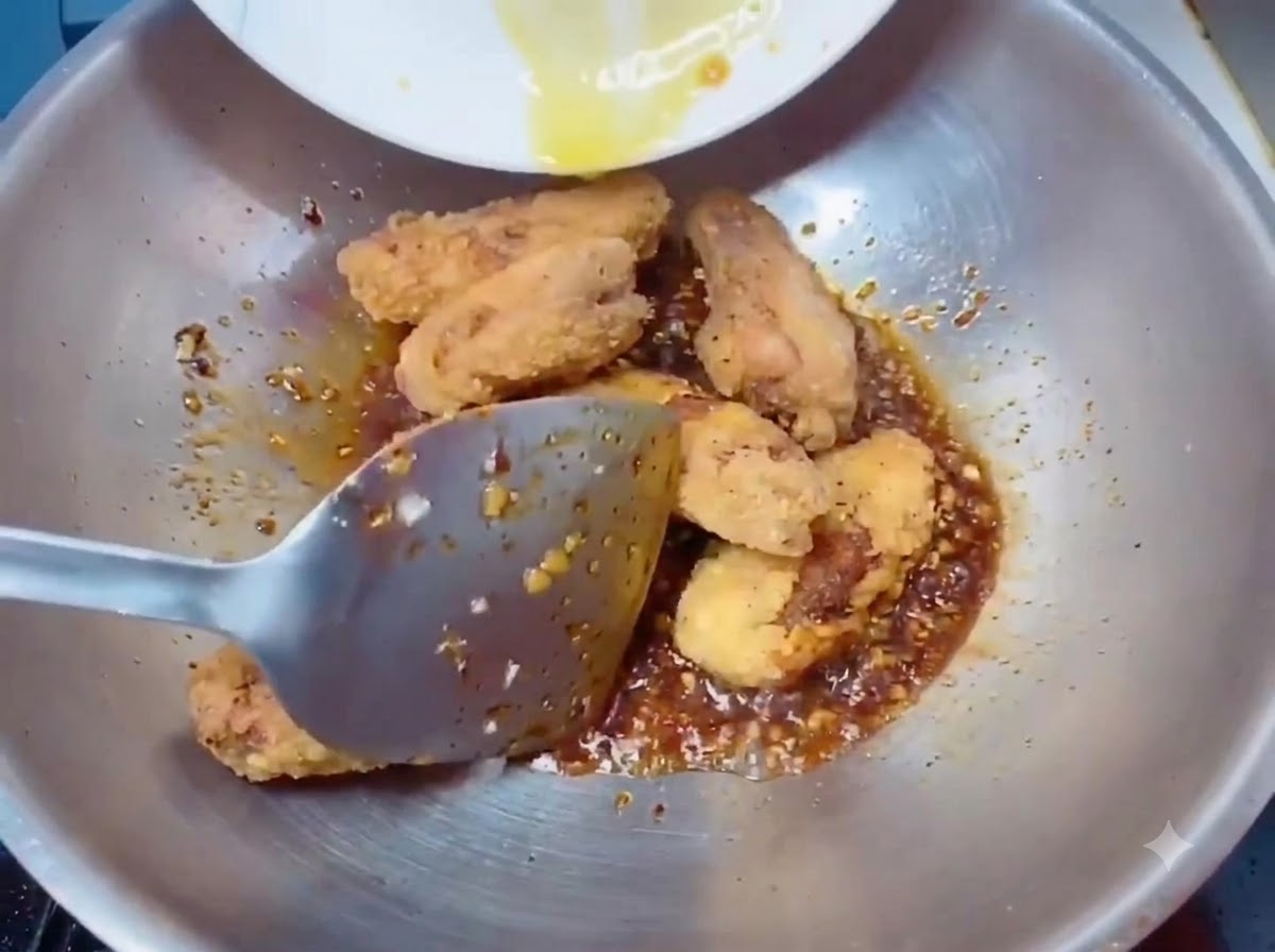 Ailes de poulet frites dorées et croustillantes transférées dans le wok avec la sauce à laide dune spatule.